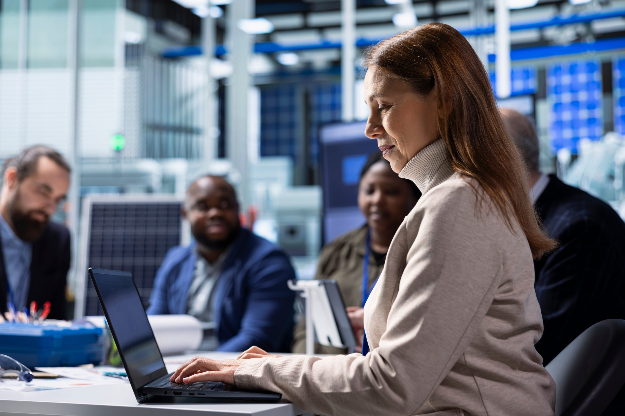 Uma mulher, em uma reunião com várias pessoas, trabalhando em um notebook.